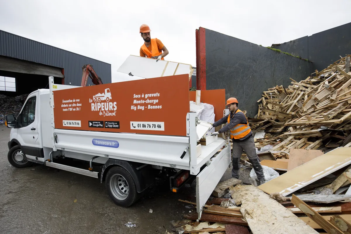Camion plateau Les Ripeurs, deux ripeurs déchargeant devant un tas de palettes