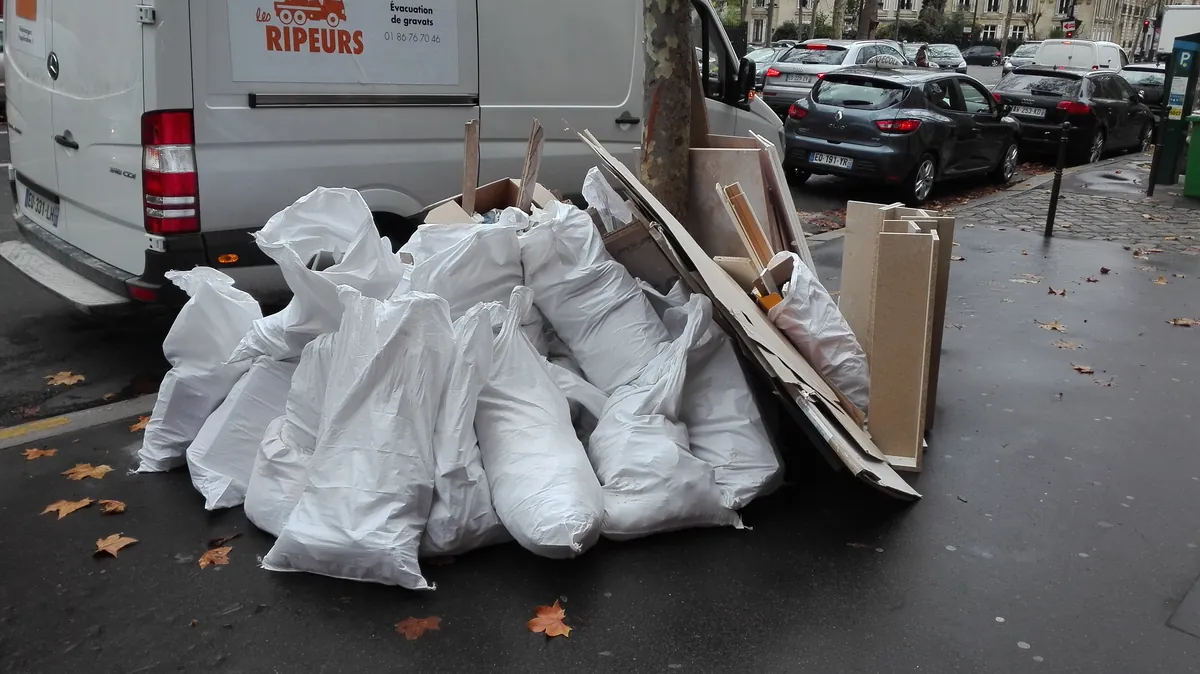 Camionnette Les Ripeurs garée le long d'un trottoir parisien, sacs à gravats et panneaux de bois en attente de chargement