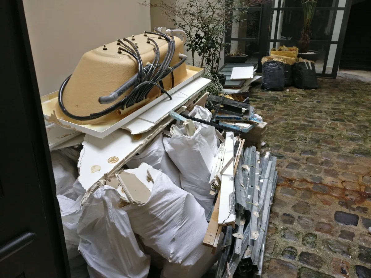Cour d'immeuble pavée avec baignoire balnéo, receveur de douche, sacs blancs et rails de placo regroupés