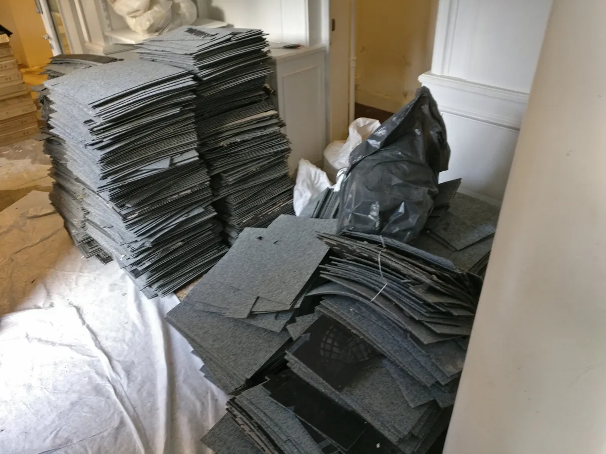 Piles de dalles de moquette grises déposées dans un appartement, sac noir et sac blanc au sol