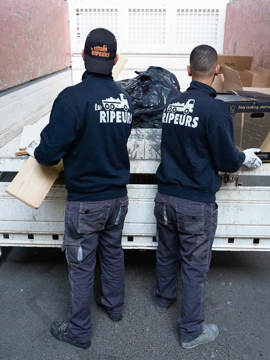 Ripeur chargeant une planche sur le plateau d'un camion, second ripeur en arrière-plan