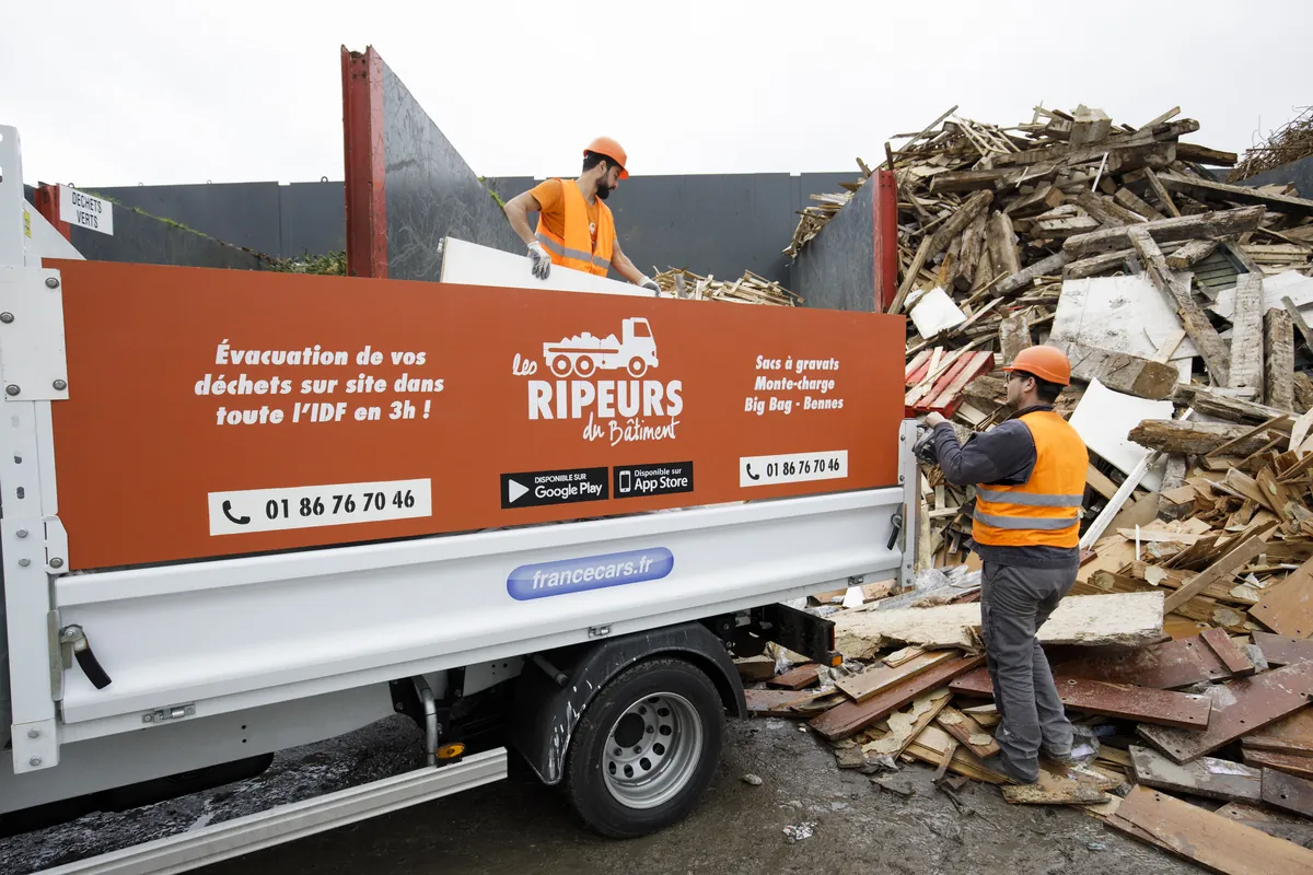 Deux ripeurs déchargeant des panneaux de bois depuis un camion plateau, sur une plateforme de valorisation