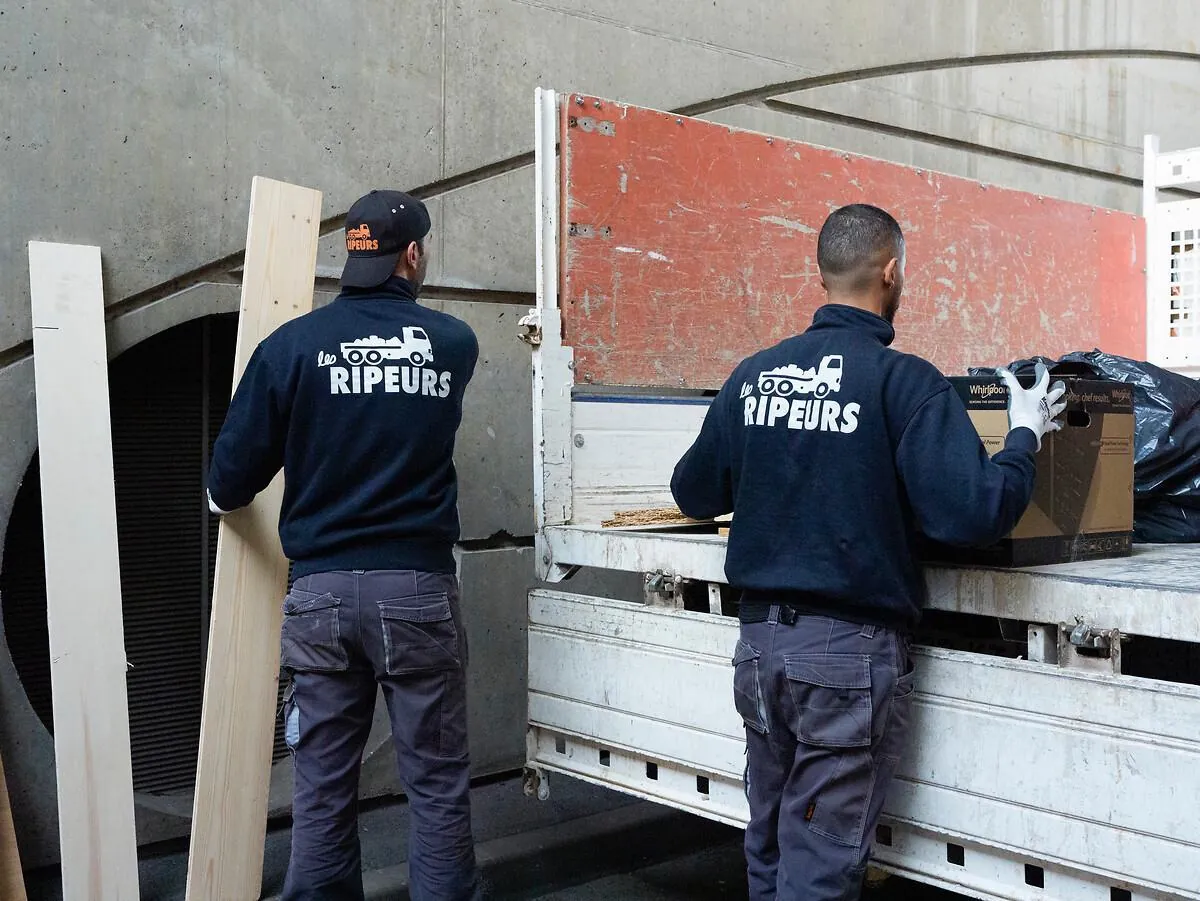 Deux ripeurs portant un carton vers un camion plateau Les Ripeurs