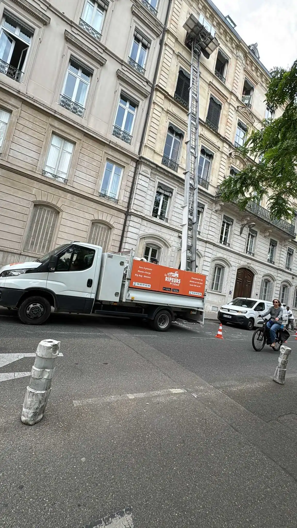 Camion plateau Les Ripeurs avec monte-charge déployé jusqu'au dernier étage d'un immeuble en pierre