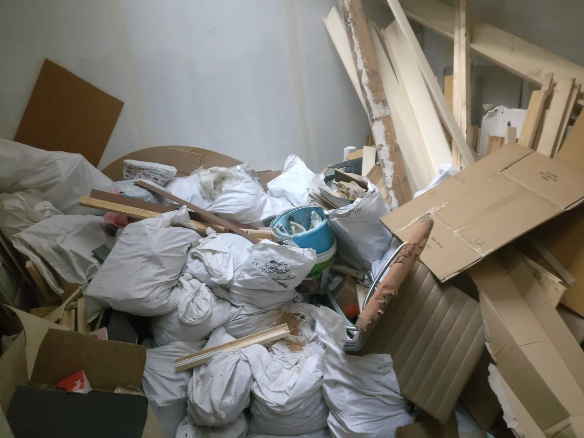 Pièce en rénovation encombrée de sacs blancs, cartons et chutes de bois, déchets en vrac non triés